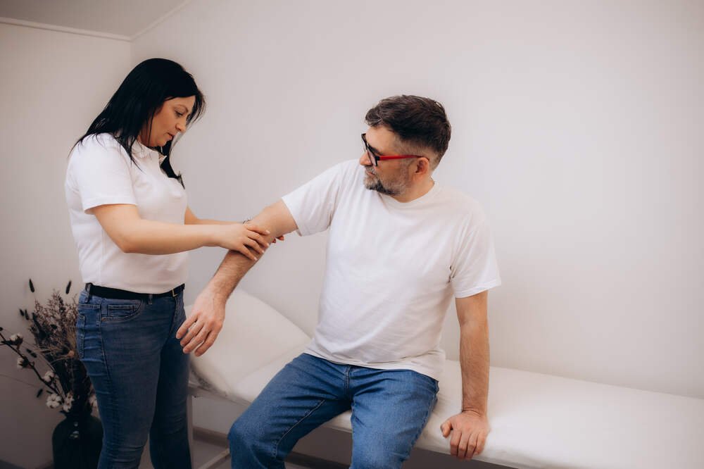 Female Physiotherapist examines male patient arm. Medazur Medical Clinic in Leytonstone.