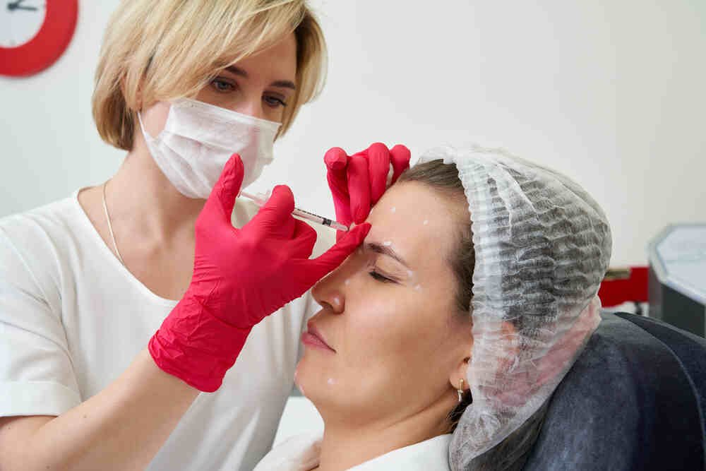 Female cosmetic doctor injects female patient in the forehead. Medazur Medical Clinic.