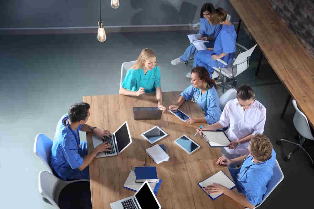Group of medical staffs sitting at table together with devices. Medazur Medical Clinic in Leytonstone.