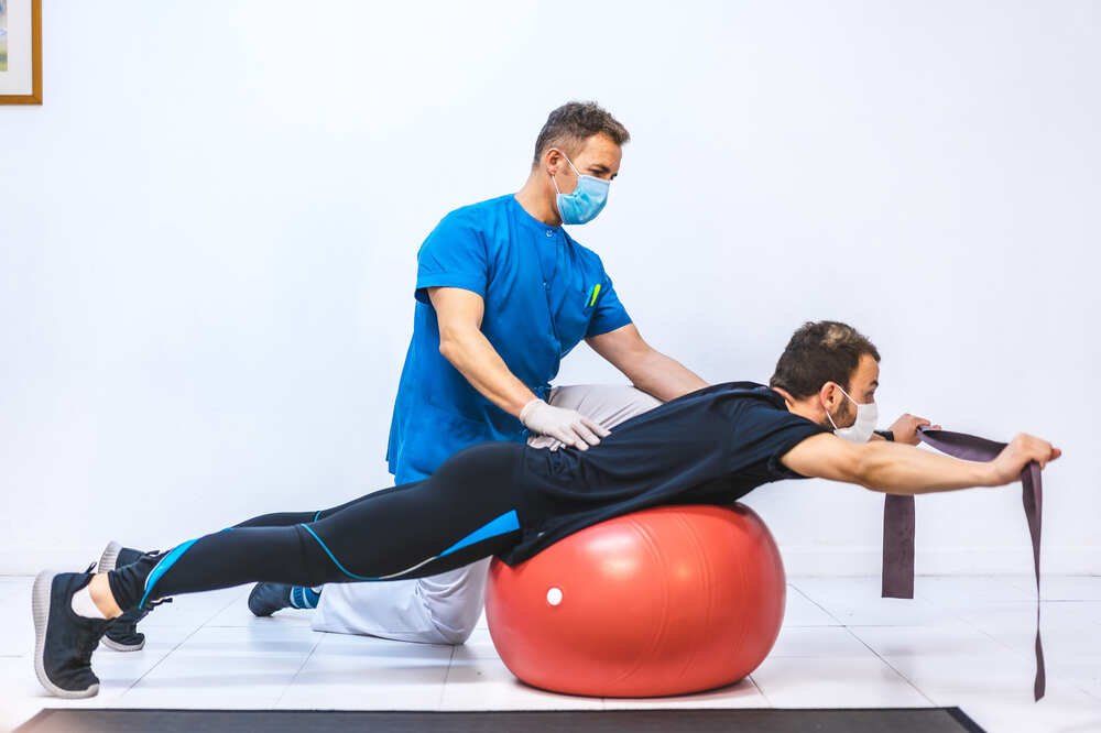 Physiotherapist With Mask Patient Doing Exercises With Rubber Giant Ball. Medazur Medical Clinic in Leytonstone.